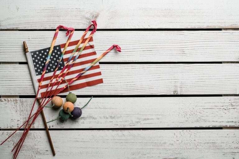 American flag with sparklers and firecrackers on a wooden surface, symbolizing patriotism and festivity.