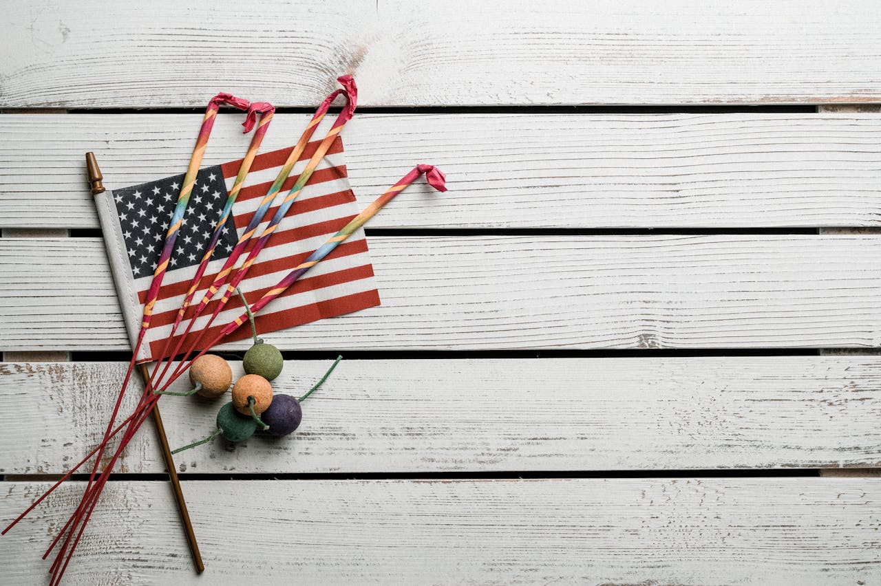 American flag with sparklers and firecrackers on a wooden surface, symbolizing patriotism and festivity.